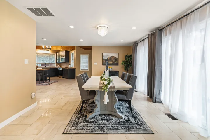Spacious dining area featuring neutral-toned tile flooring, recessed lighting, and a crystal chandelier