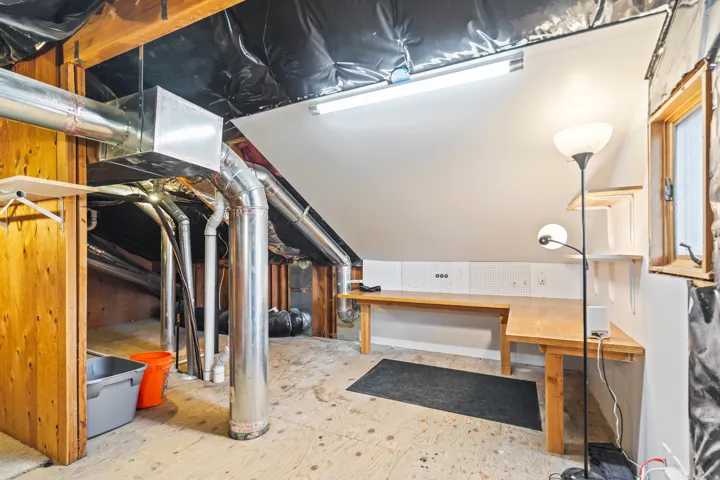 Finished attic space featuring exposed wood framing, built-in shelving, a wood-finish workbench, and a fixed window
