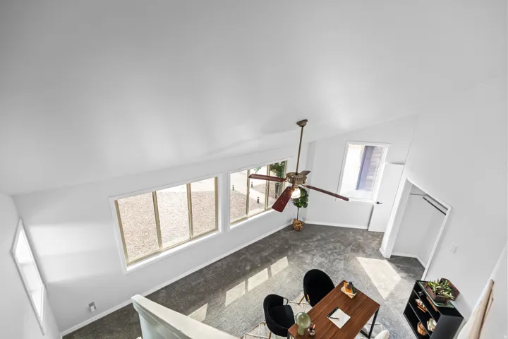 Vaulted white ceiling with a ceiling fan, multiple windows with white trim, and a built-in closet with hanging rods