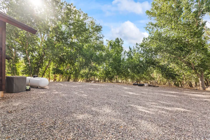 Gravel parking area featuring mature trees and a propane tank