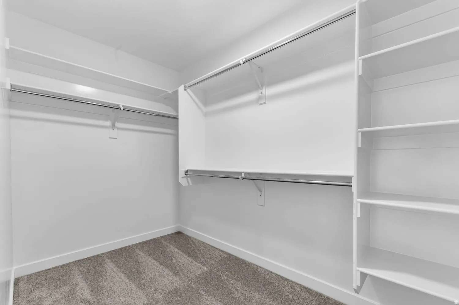 Spacious closet featuring white shelving, multiple hanging rods, and grey patterned carpeting