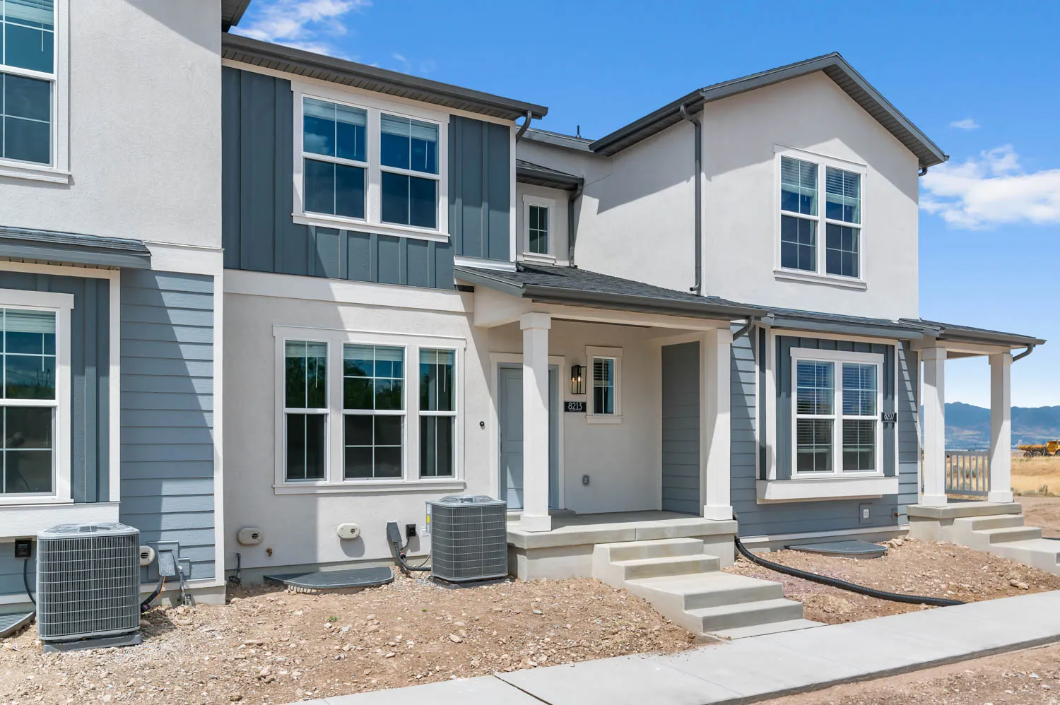 Contemporary townhouse facade featuring a covered entry porch, white framed windows, board and batten siding accents, stucco exterior, and concrete steps
