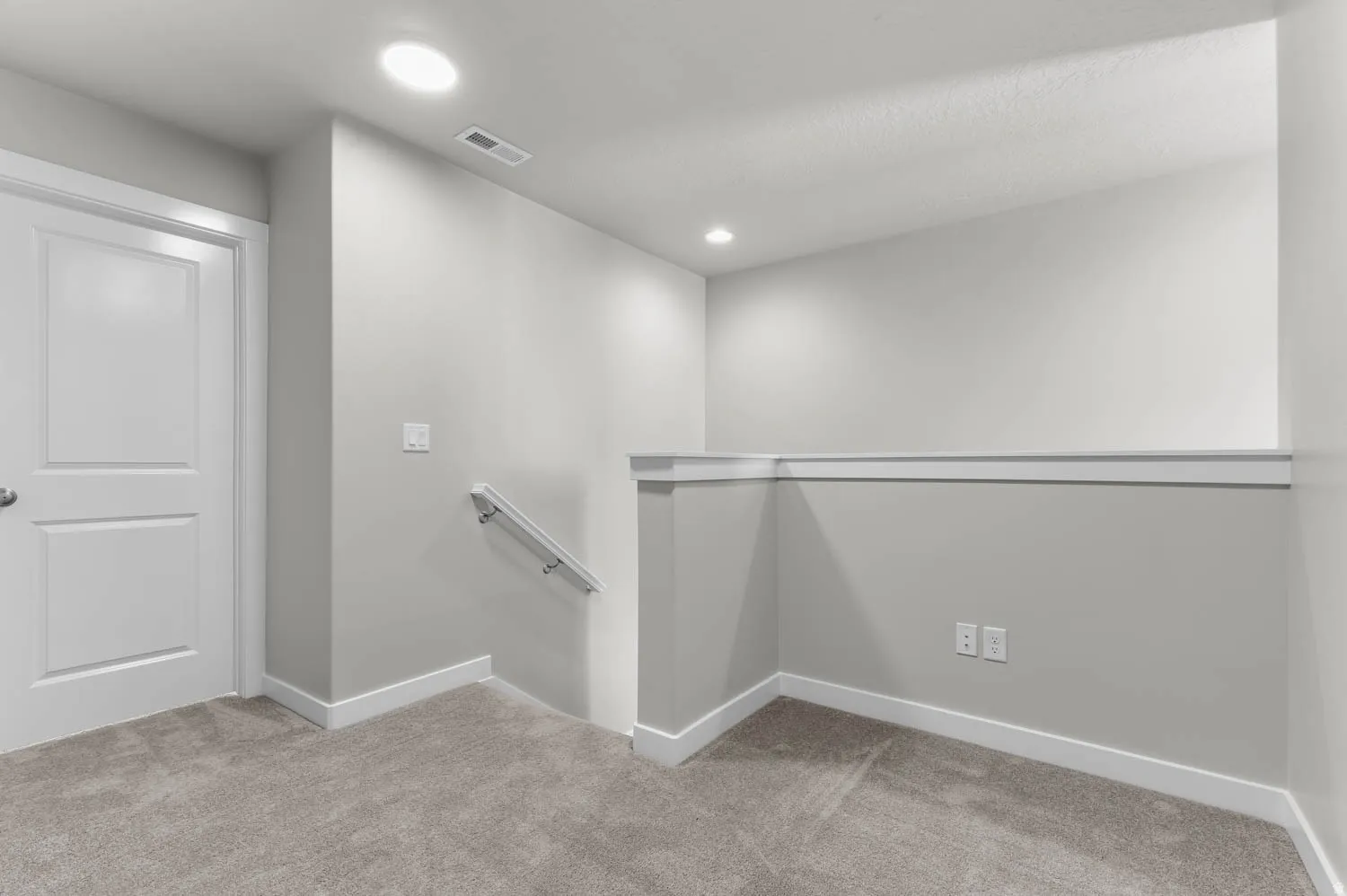 Carpeted landing area featuring a white paneled door, recessed lighting, and a white wall-mounted handrail