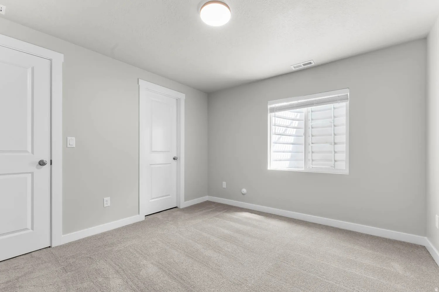 Neutral tone walls with white trim, gray carpet flooring, ceiling light fixture, and window with white plantation shutters