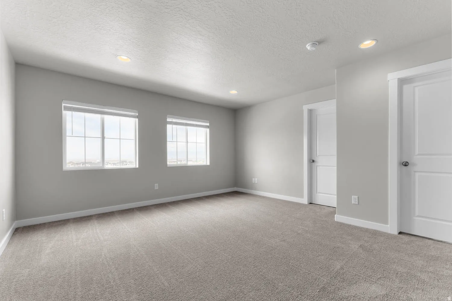 Spacious room featuring neutral carpeting, light gray wall paint, and white trim