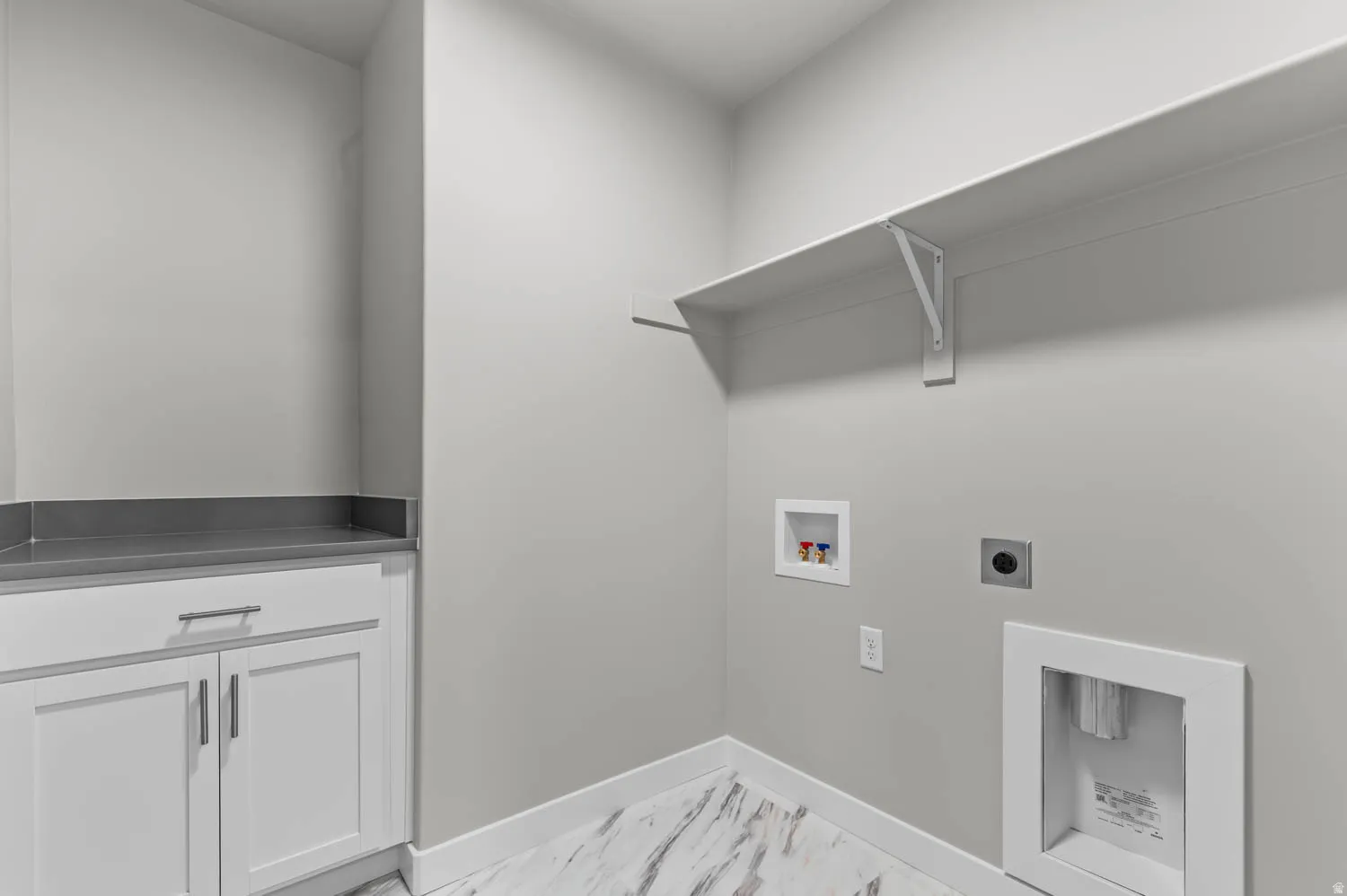 Laundry area featuring white shaker-style cabinetry with chrome hardware, a dark gray countertop, and an upper storage shelf