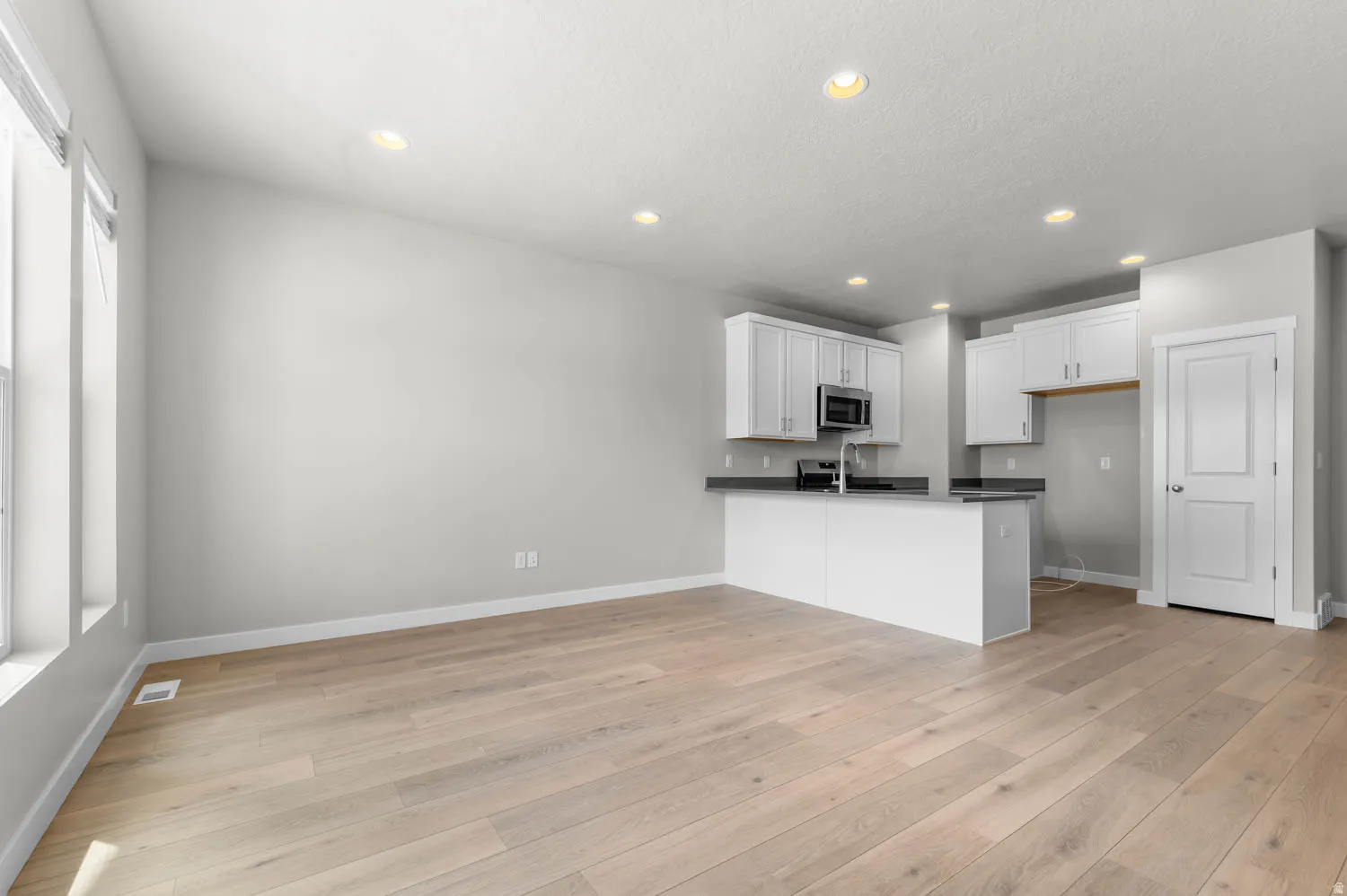 Open-concept living area featuring light wood-finish flooring, recessed lighting, and a kitchen with white cabinetry