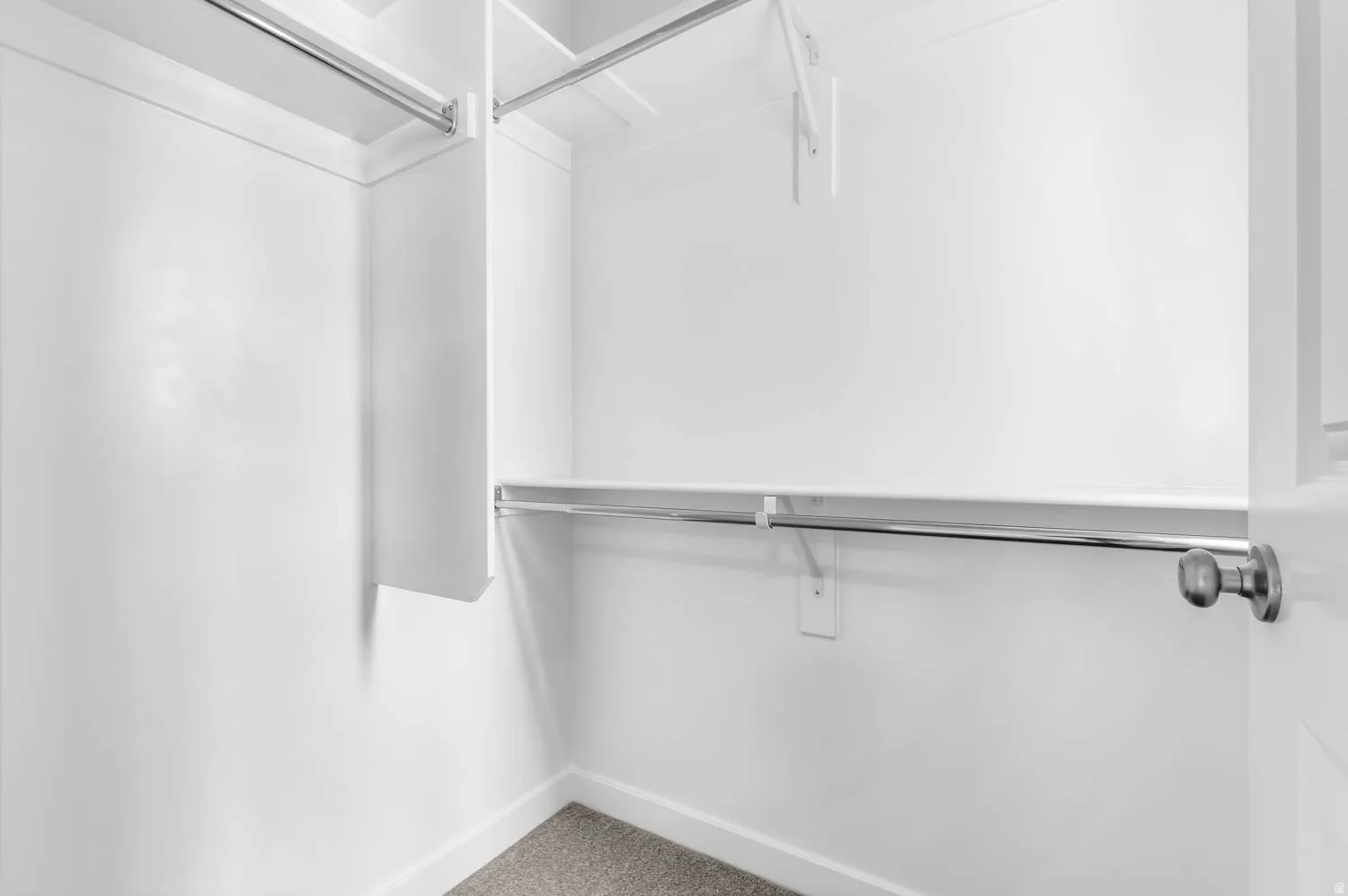 Walk-in closet featuring white walls, white shelving, multiple chrome hanging rods, and gray carpet flooring