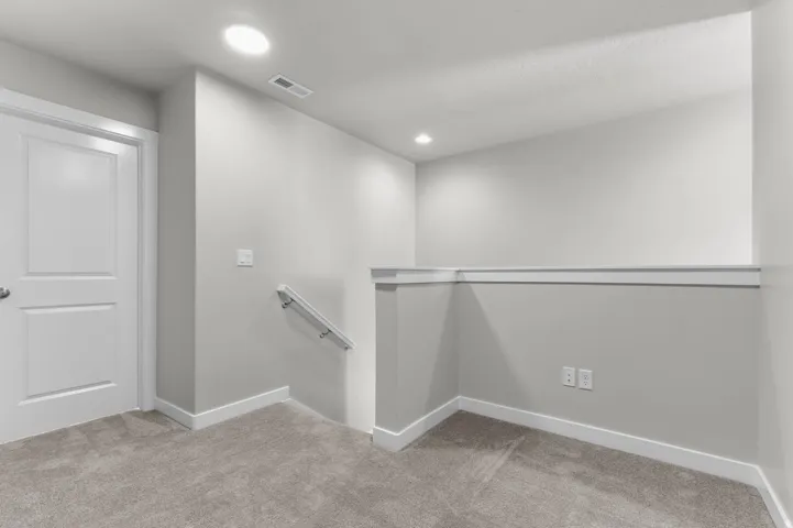 Carpeted landing area featuring a white paneled door, recessed lighting, and a white wall-mounted handrail