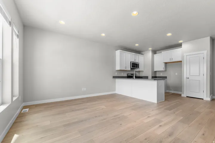 Open-concept living area featuring light wood-finish flooring, recessed lighting, and a kitchen with white cabinetry