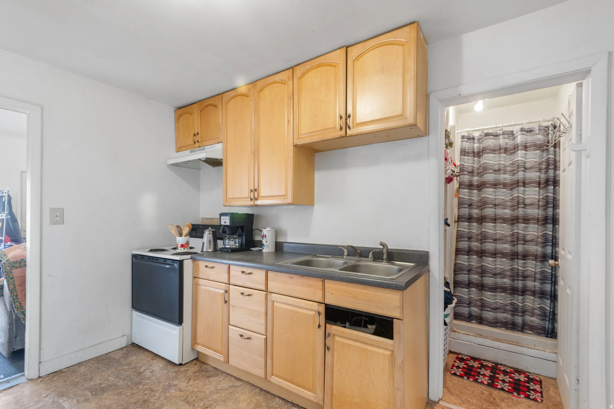 Compact kitchen featuring light wood cabinetry, a dual-basin stainless steel sink, and a built-in range with an overhead exhaust hood