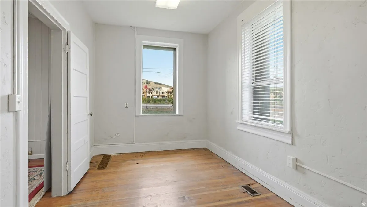 Light-filled room featuring wood-finish flooring, two windows, and a white paneled door