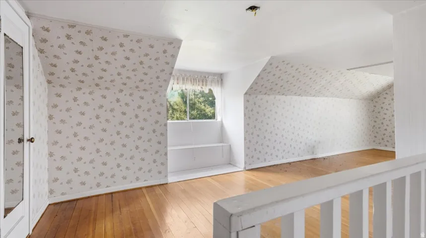 Spacious room featuring wood-finish flooring, sloped ceilings, and patterned wallpaper