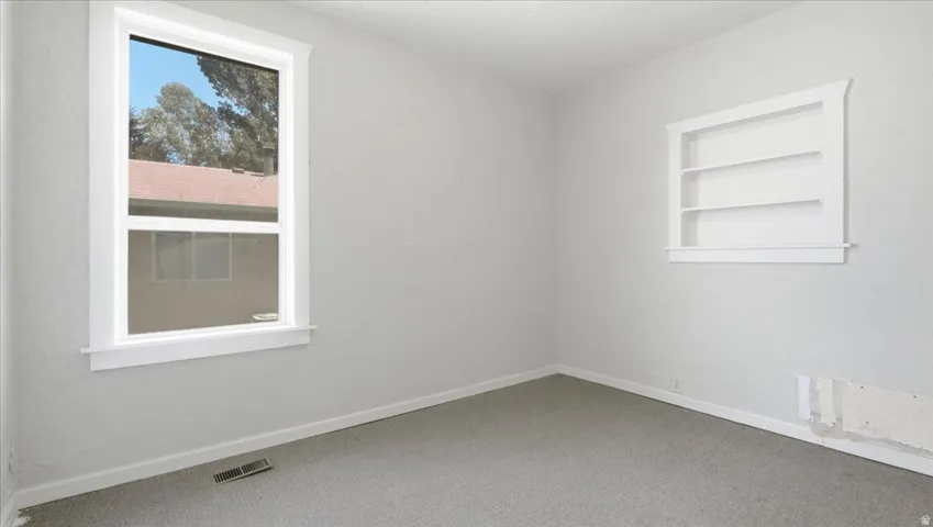 Light-toned room featuring a window with white trim, a built-in wall shelf, and gray carpet flooring