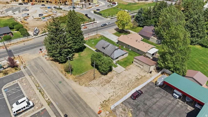 Aerial perspective of a property featuring a central residence, a separate accessory building, mature trees, and a substantial paved area