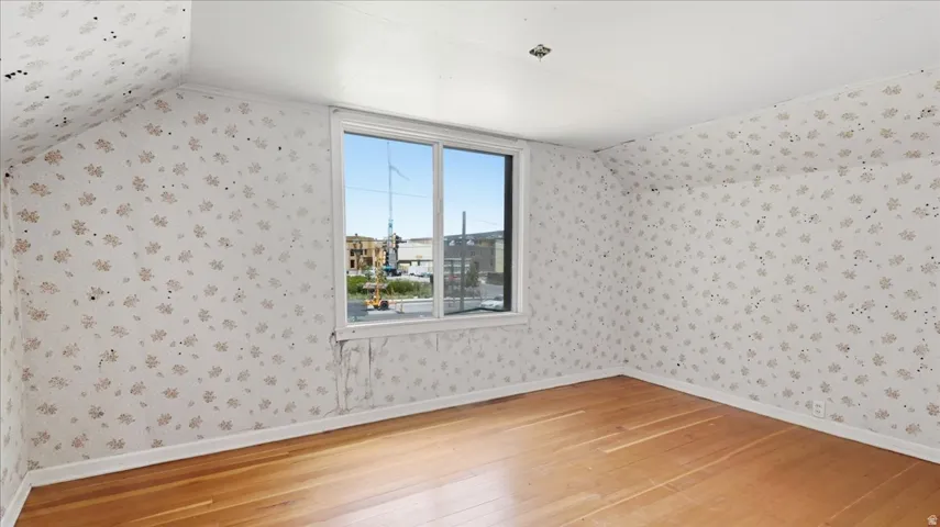 Room featuring wood-finish flooring, a window offering exterior views, white baseboards, and a patterned wallpaper