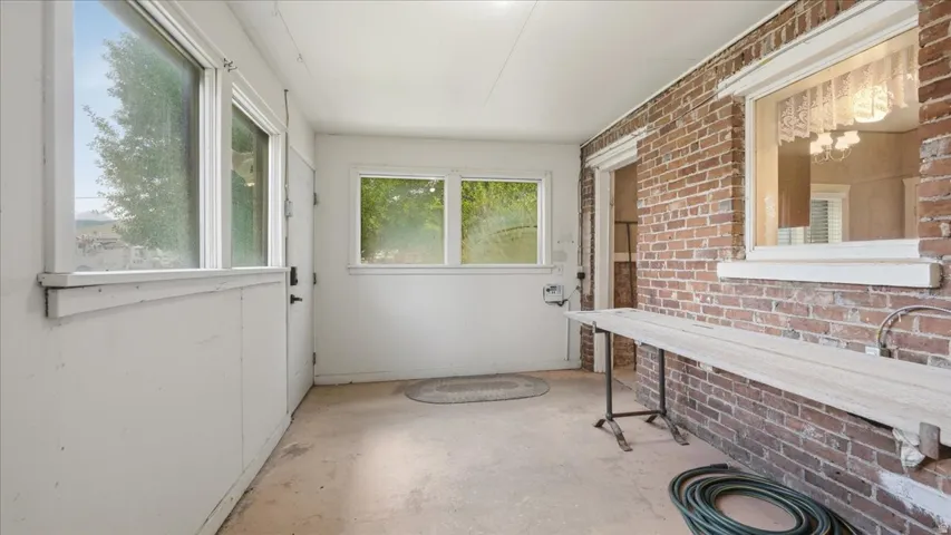 Enclosed porch featuring exposed brick wall, multiple windows, a rear entry door, and a built-in workbench