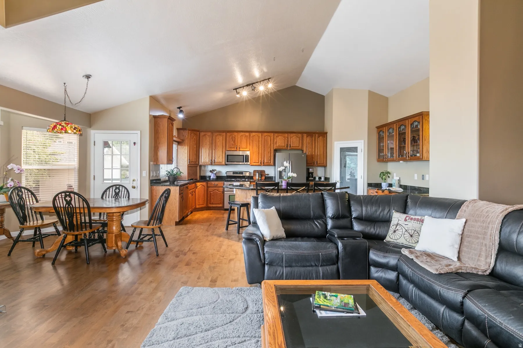 Open concept living area featuring vaulted ceilings, wood-finish flooring, a kitchen with rich wood cabinetry, and a dining area with a decorative pendant light