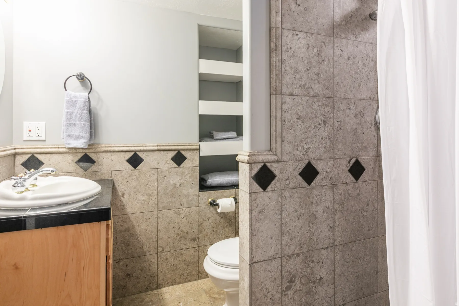 Tiled bathroom featuring a light wood-finish vanity with a black countertop and integrated sink