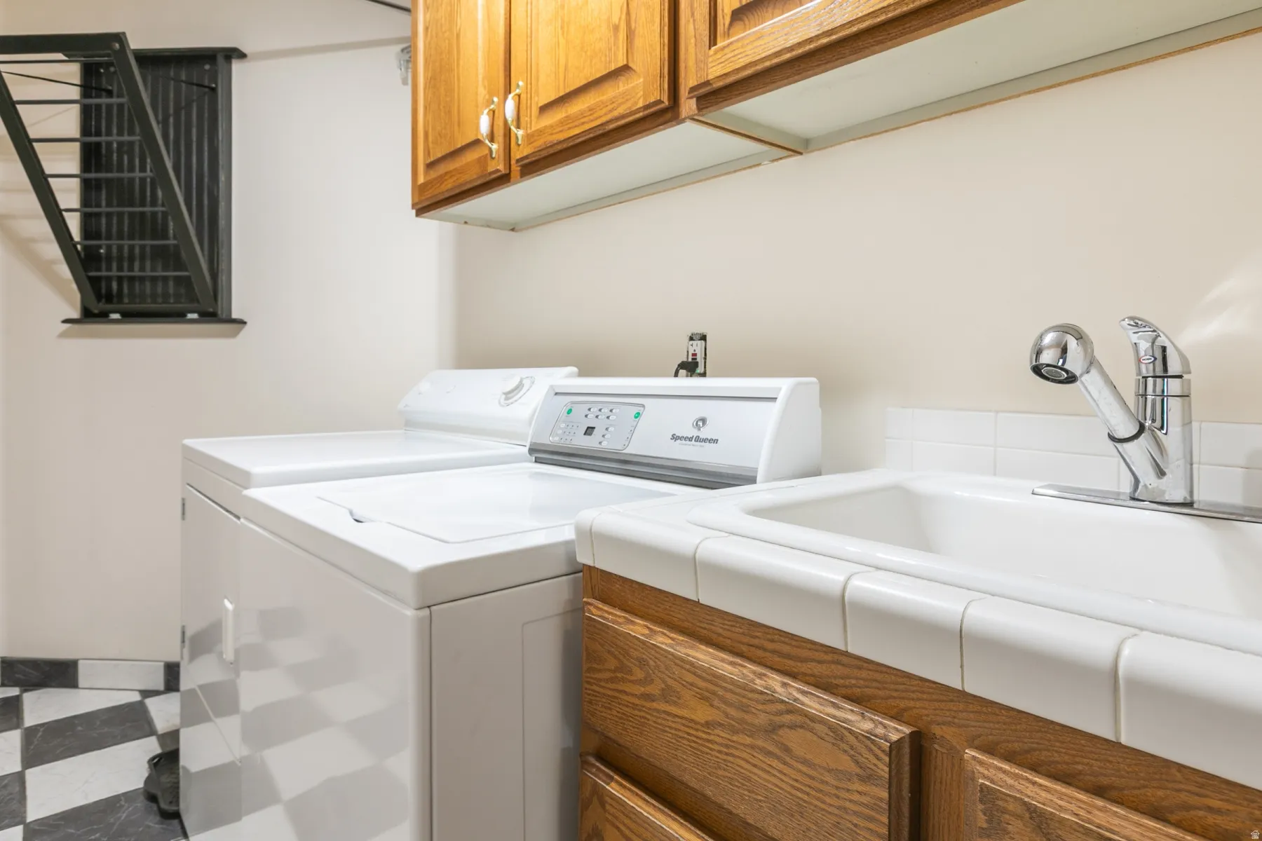 Utility area featuring a ceramic tile sink with a chrome faucet, wood cabinetry, and checkerboard floor tiling