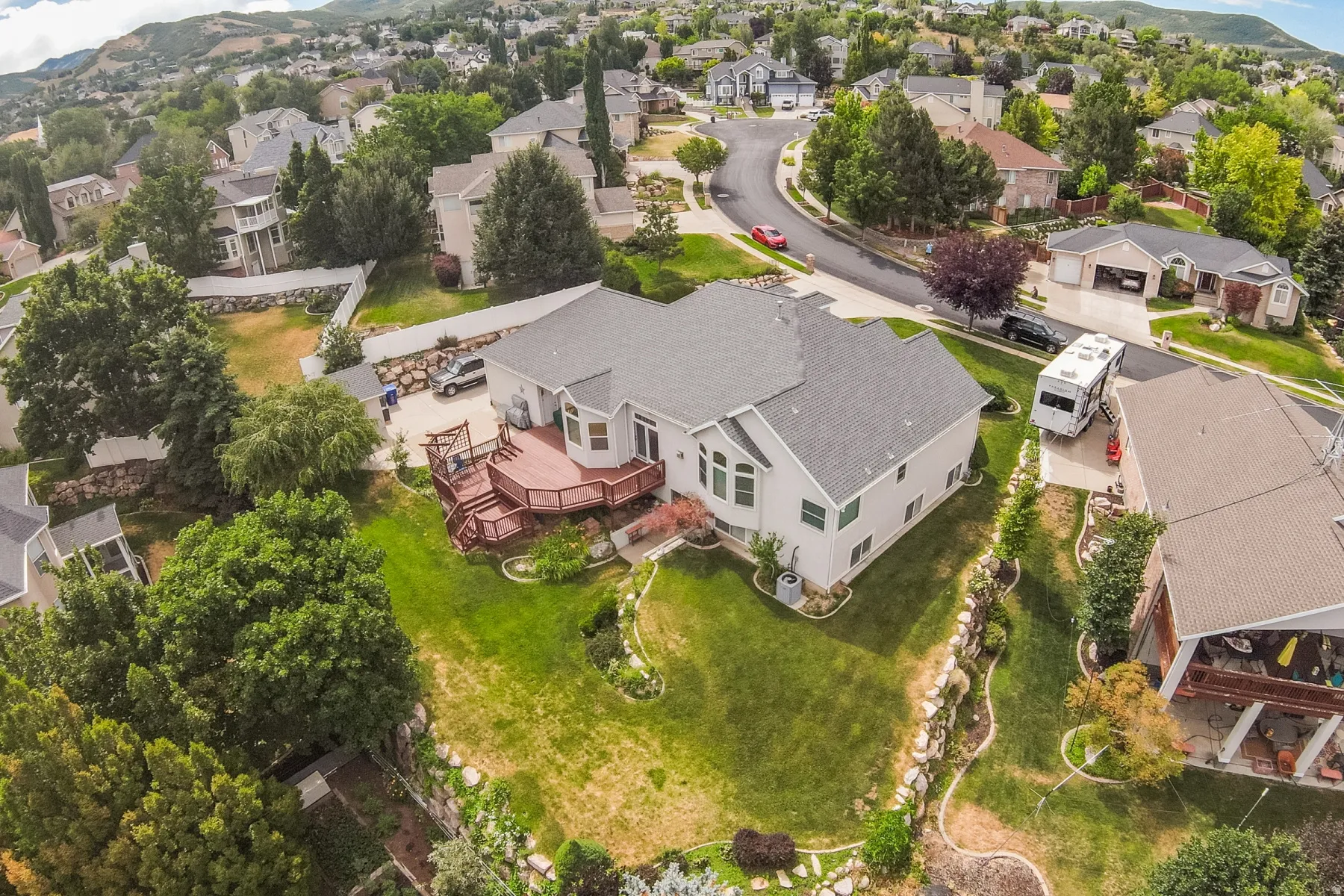 Expansive rear exterior featuring a multi-level wood deck, abundant green space, and mature landscaping
