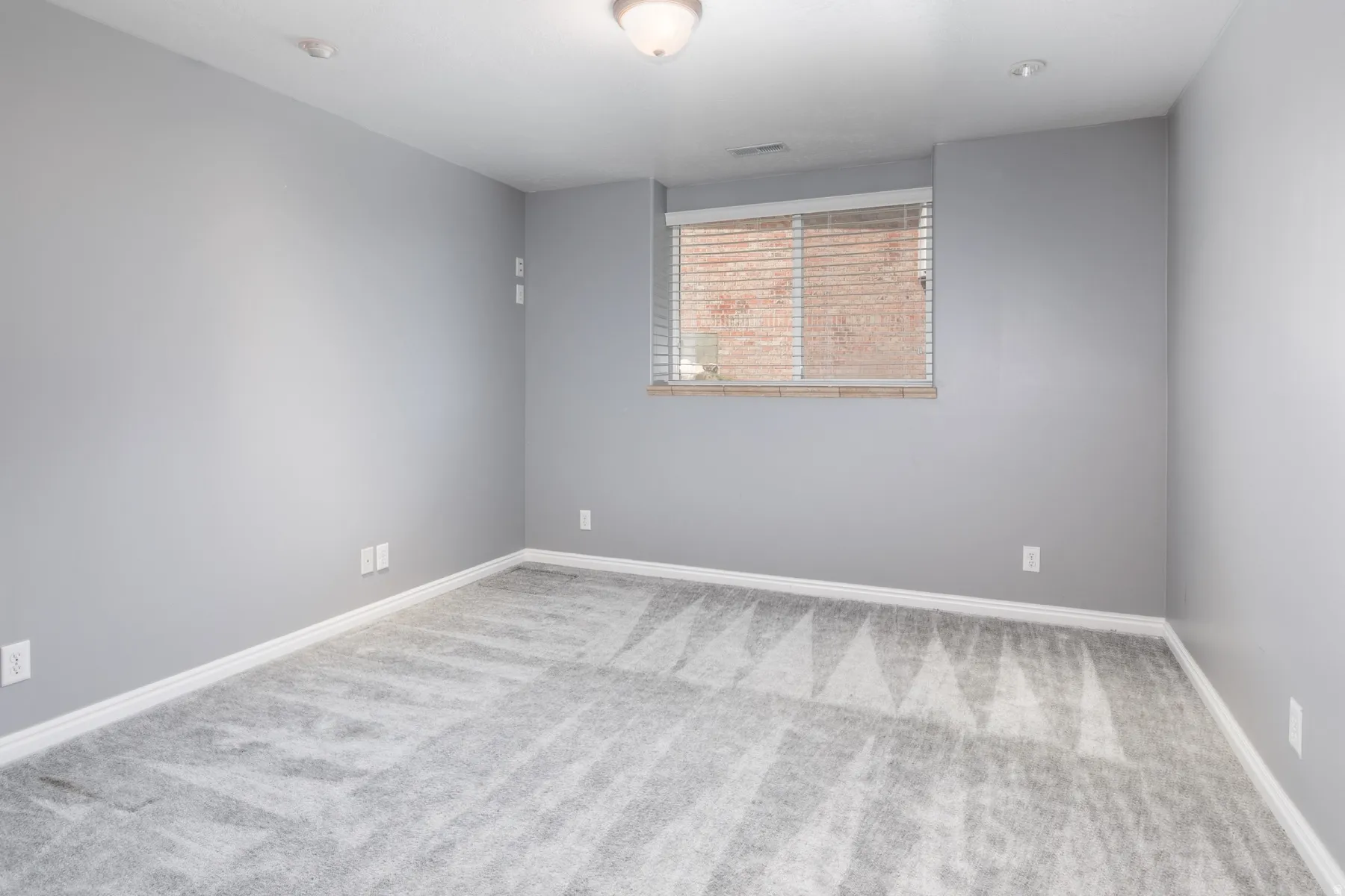 Gray patterned carpeting with white baseboards, a window featuring horizontal blinds, and a flush mount ceiling light
