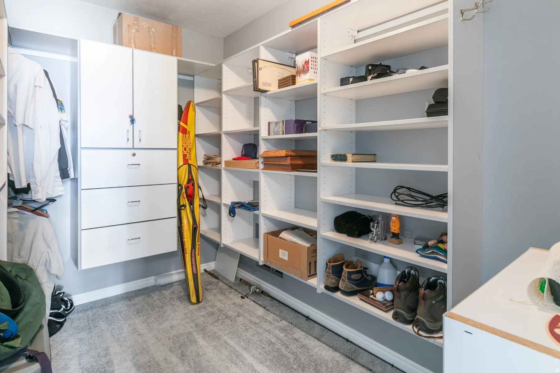 Custom closet system featuring extensive open shelving, a built-in cabinetry unit with locking doors, multiple drawers, and dedicated hanging space