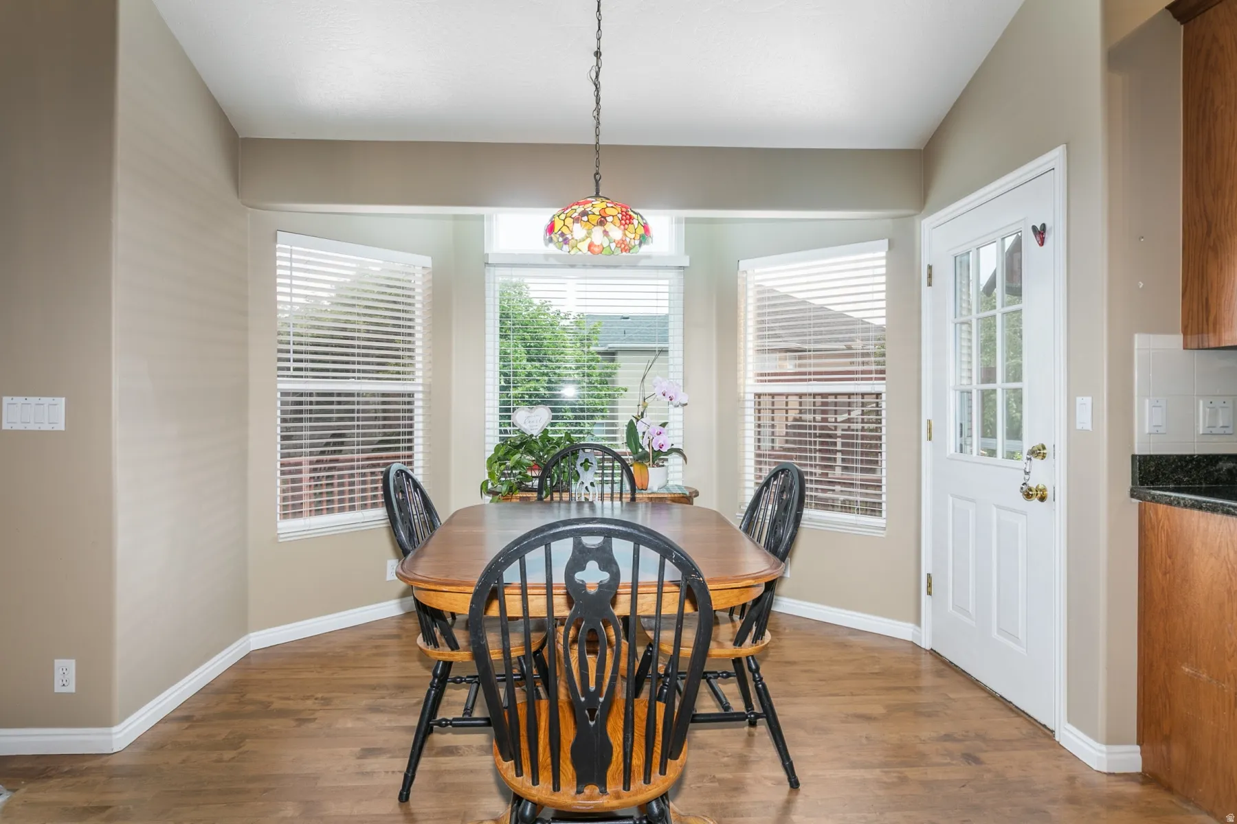 Bay window with multiple windows and blinds, wood-finish flooring, and a glass-paneled exterior door