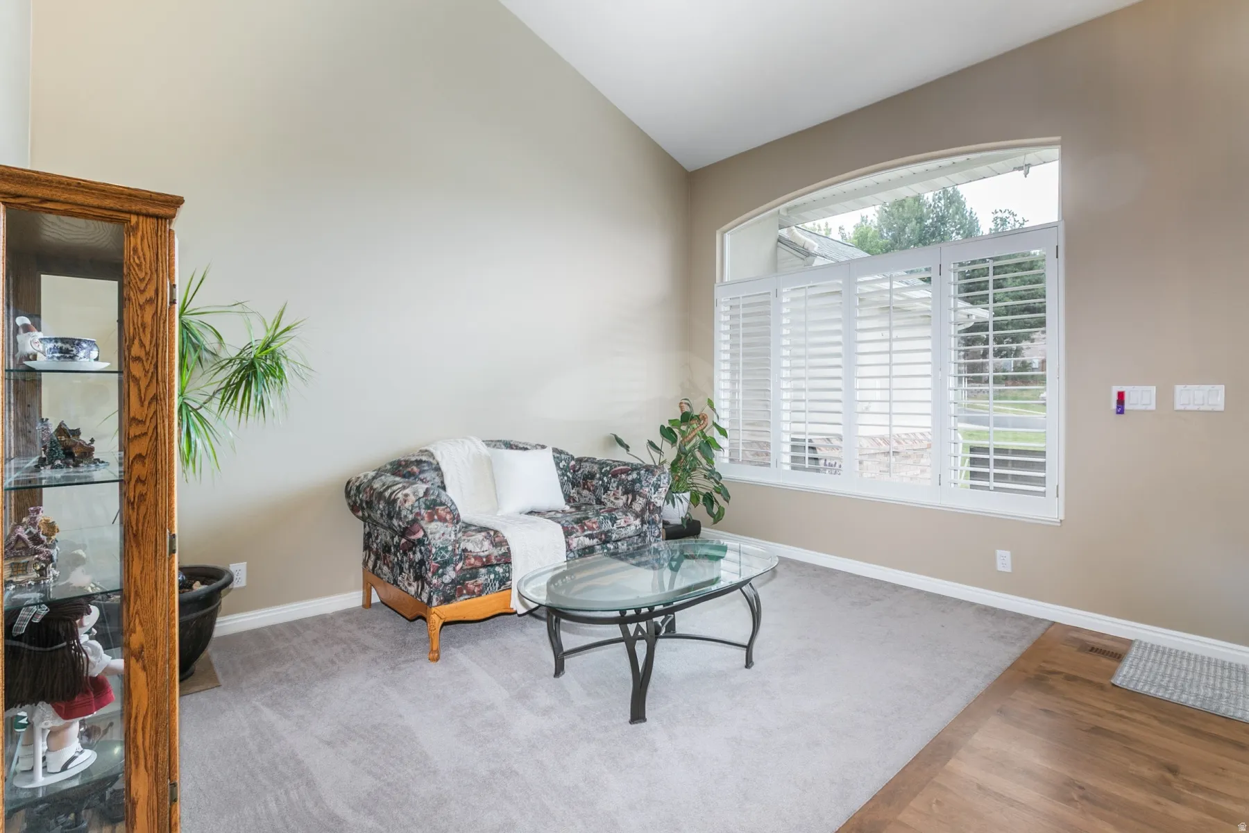 Living area featuring a vaulted ceiling and an arched window with white plantation shutters