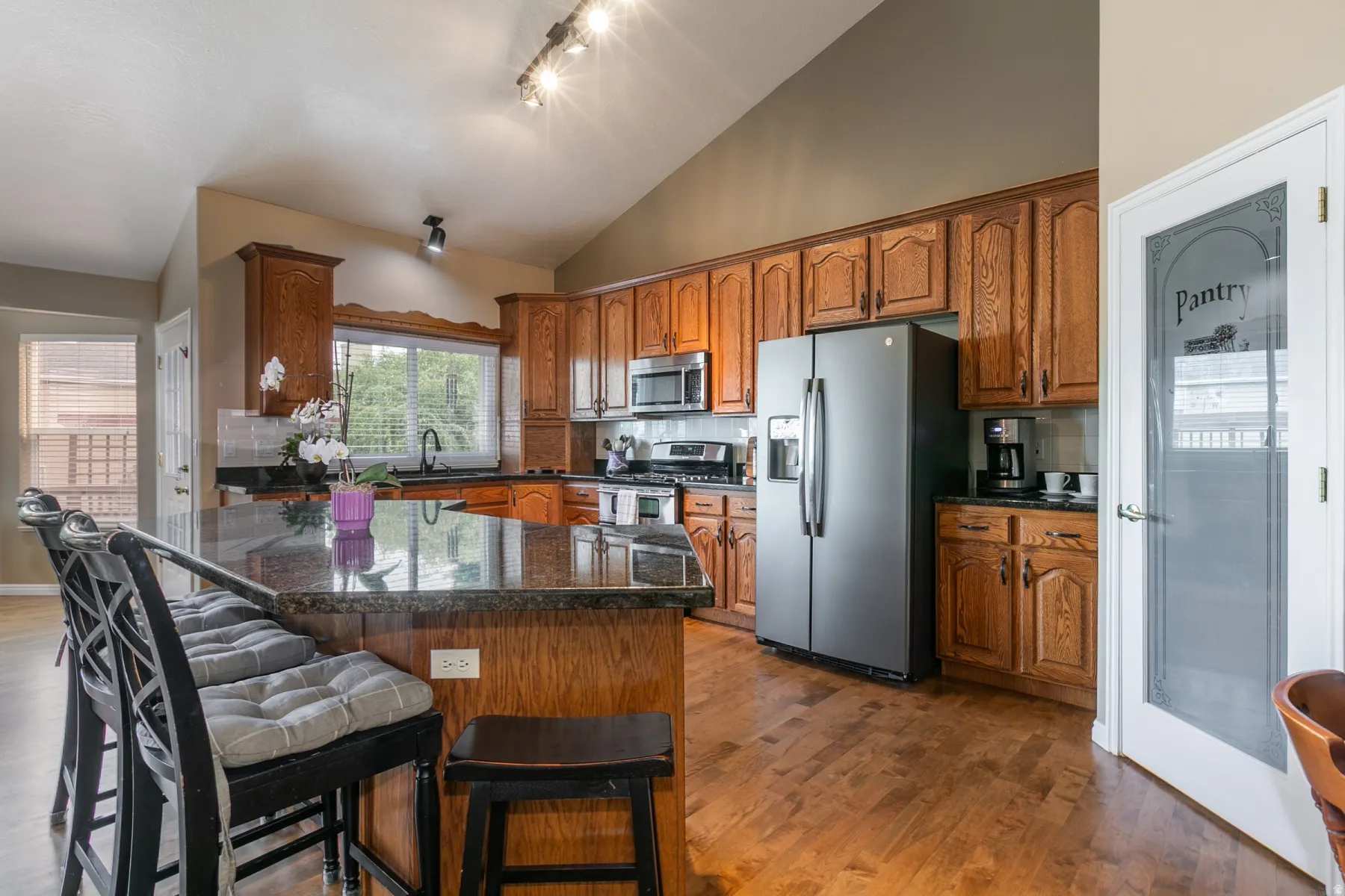 Kitchen featuring wood cabinetry, stainless steel appliances, a center island with a stone countertop, wood-finish flooring, and a vaulted ceiling