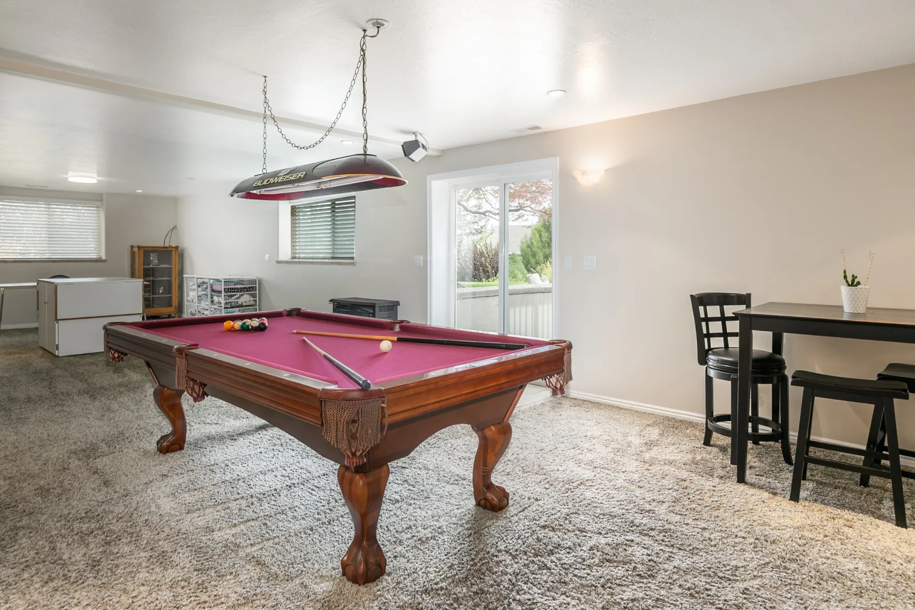 Spacious recreation room featuring a pool table with a hanging light fixture, soft carpeting, and a sliding glass door to exterior