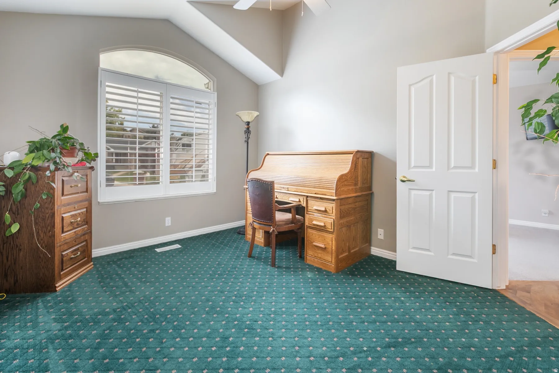 Arched window with plantation shutters, vaulted ceiling, ceiling fan, and paneled door