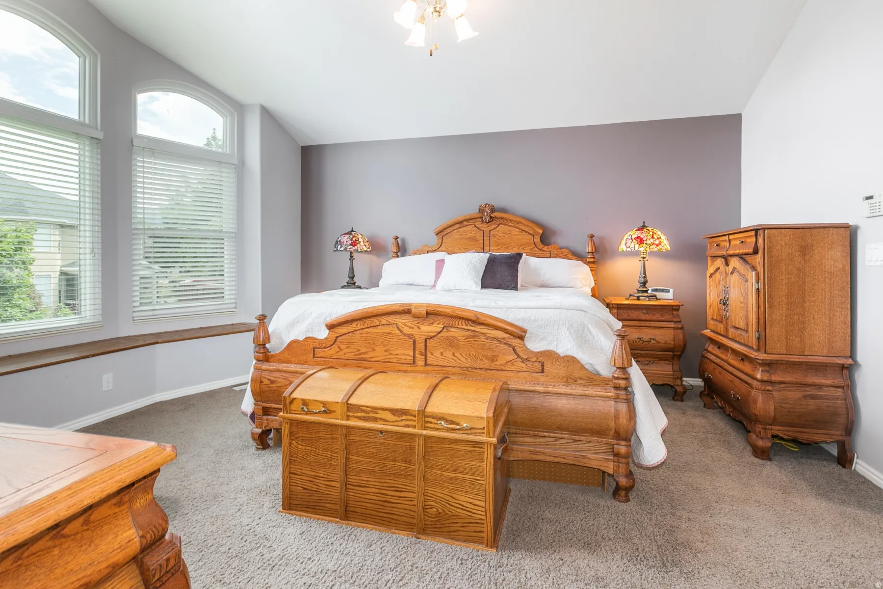 Vaulted ceiling bedroom featuring arched windows with blinds, a window seat, and carpet flooring