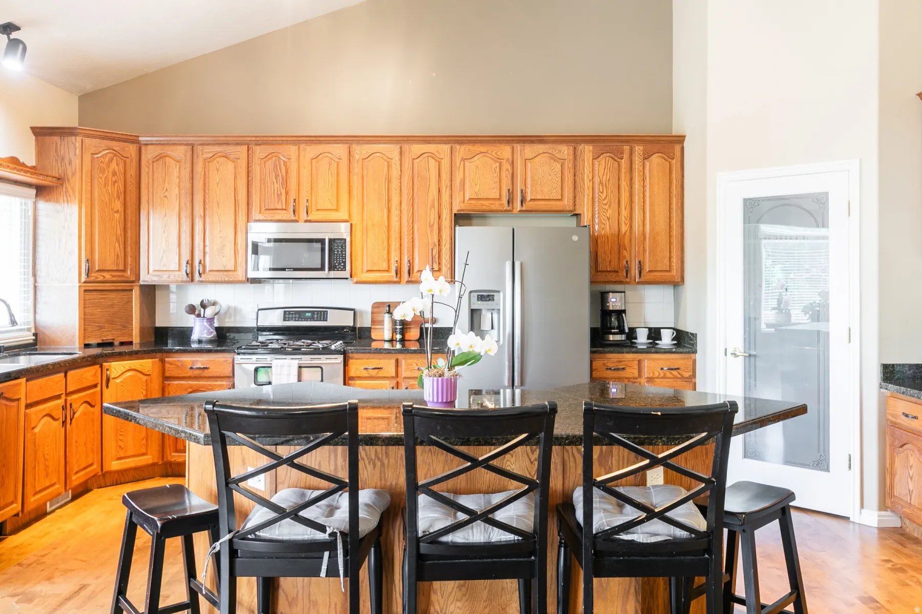 Kitchen featuring a breakfast bar with stone countertops, a full suite of stainless steel appliances, wood-finish flooring, ample cabinetry, and vaulted ceilings
