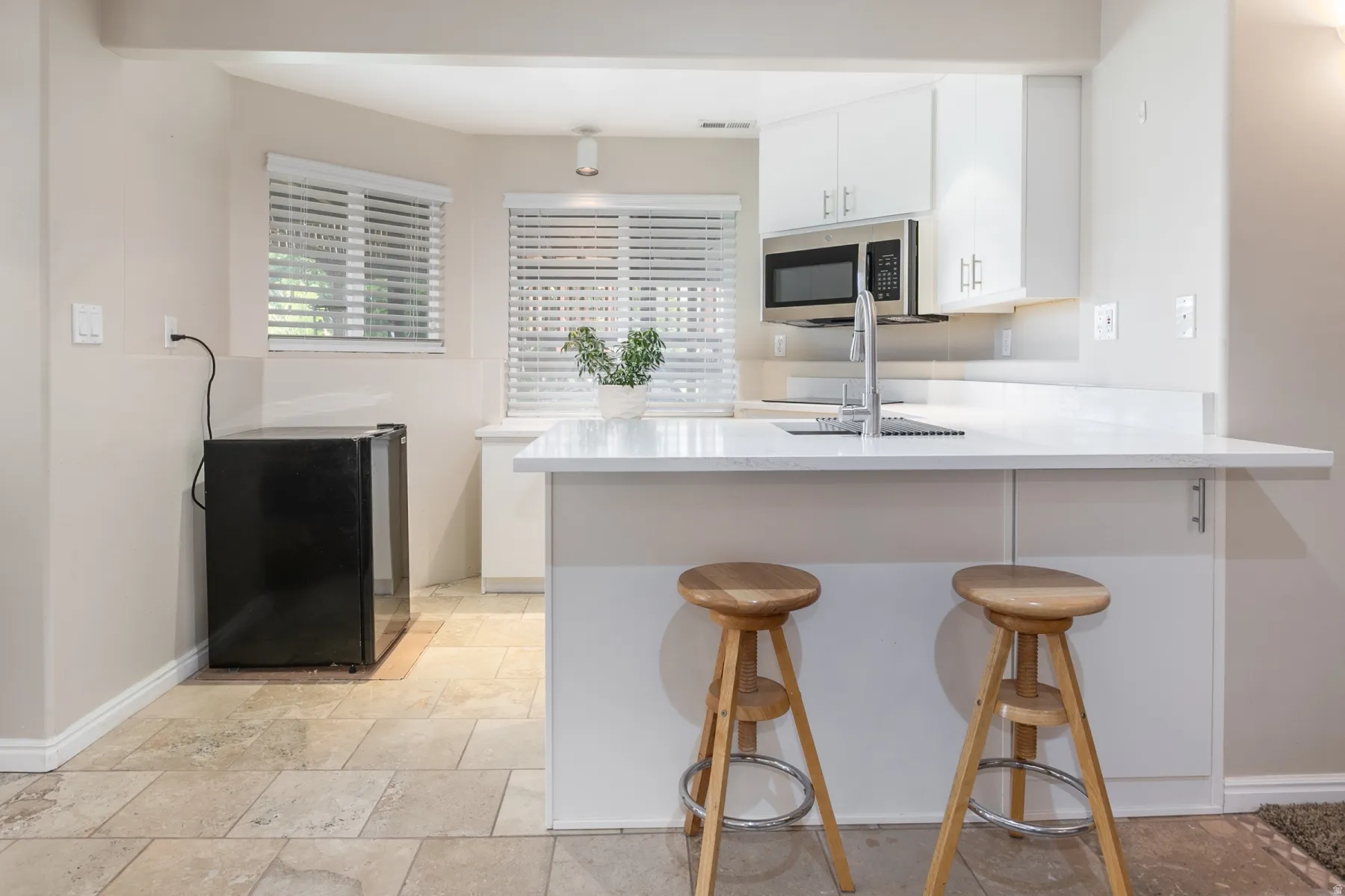 Kitchen featuring white cabinetry, stainless steel microwave, and a white countertop with an undermount sink