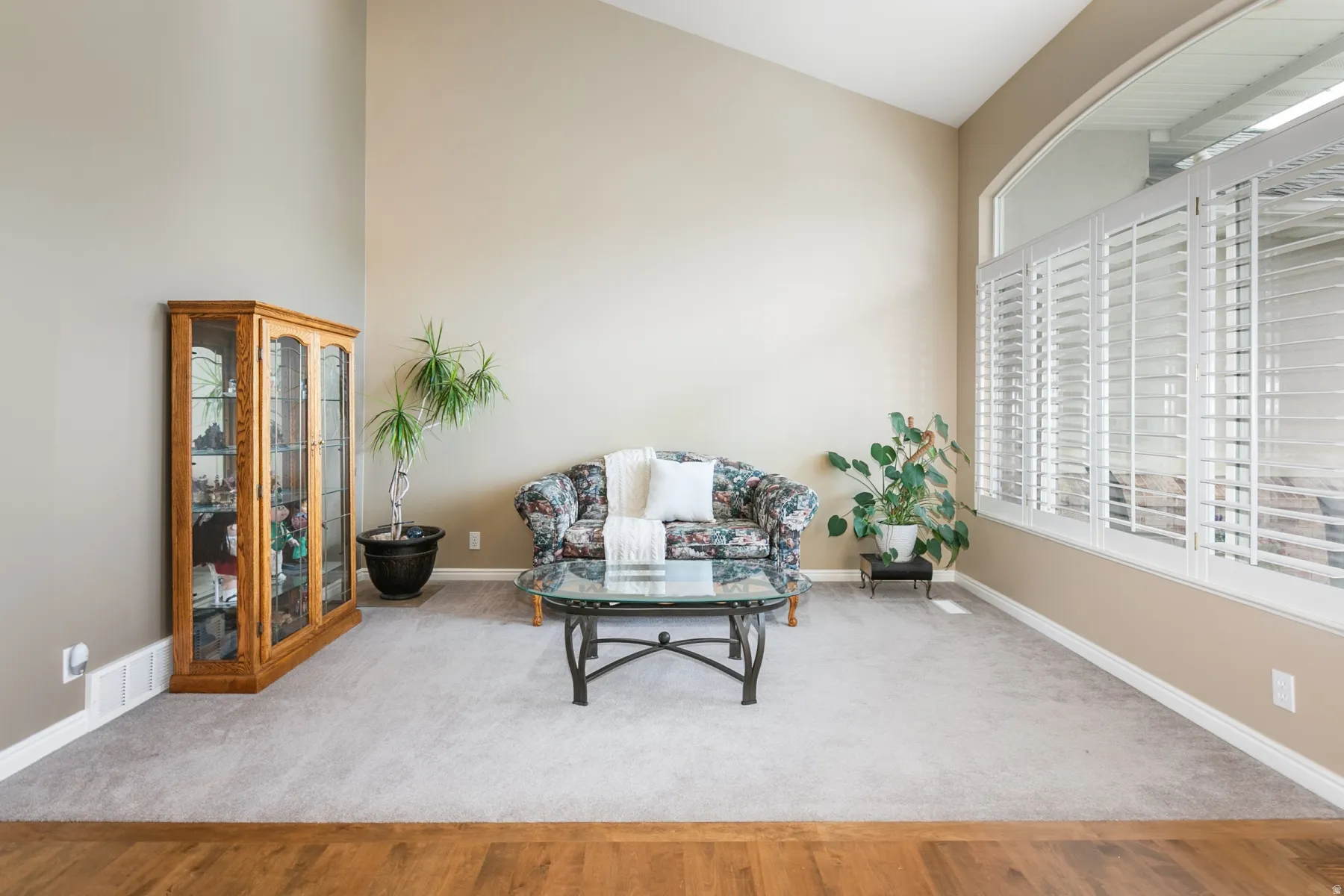 Vaulted ceiling interior featuring a large arched window with plantation shutters, light tan wall paint, and gray carpeting