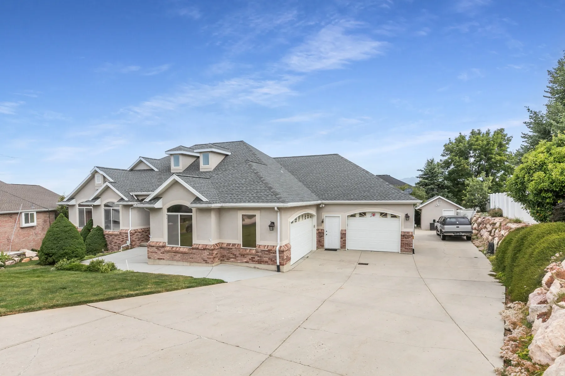Exterior facade featuring stucco siding, stone accents, multiple dormer windows, and a multi-car garage