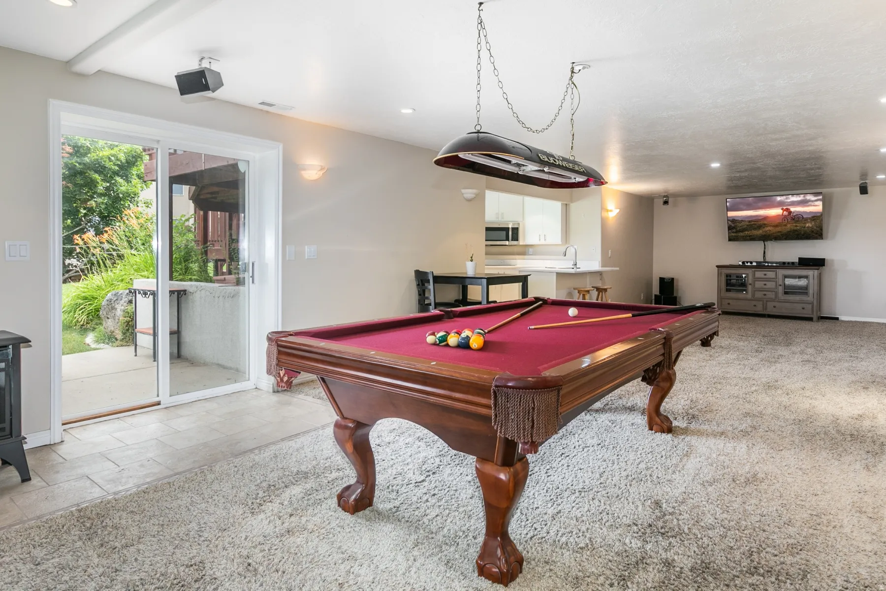 Spacious entertainment area featuring a full-sized billiard table with overhead lighting, plush carpet, and a sliding glass door providing outdoor access