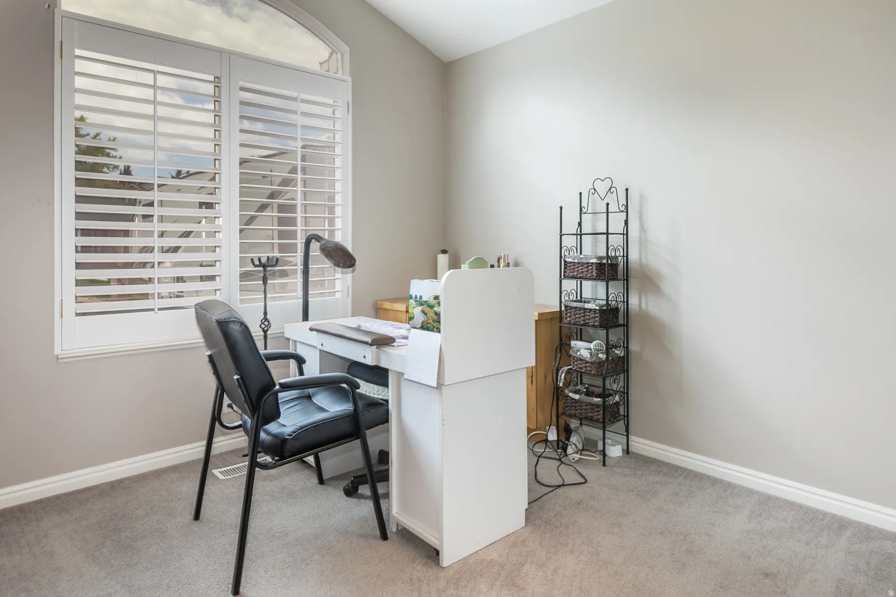 Arch-top window with white plantation shutters, soft gray wall paint, and gray carpeted flooring