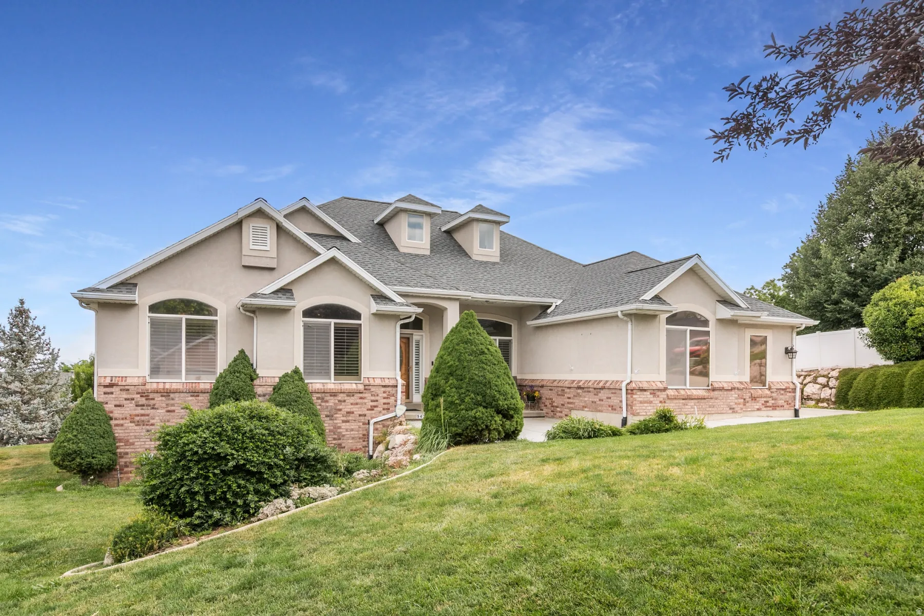 Expansive stucco and brick exterior featuring multiple dormer windows, a prominent entryway, and mature landscaping