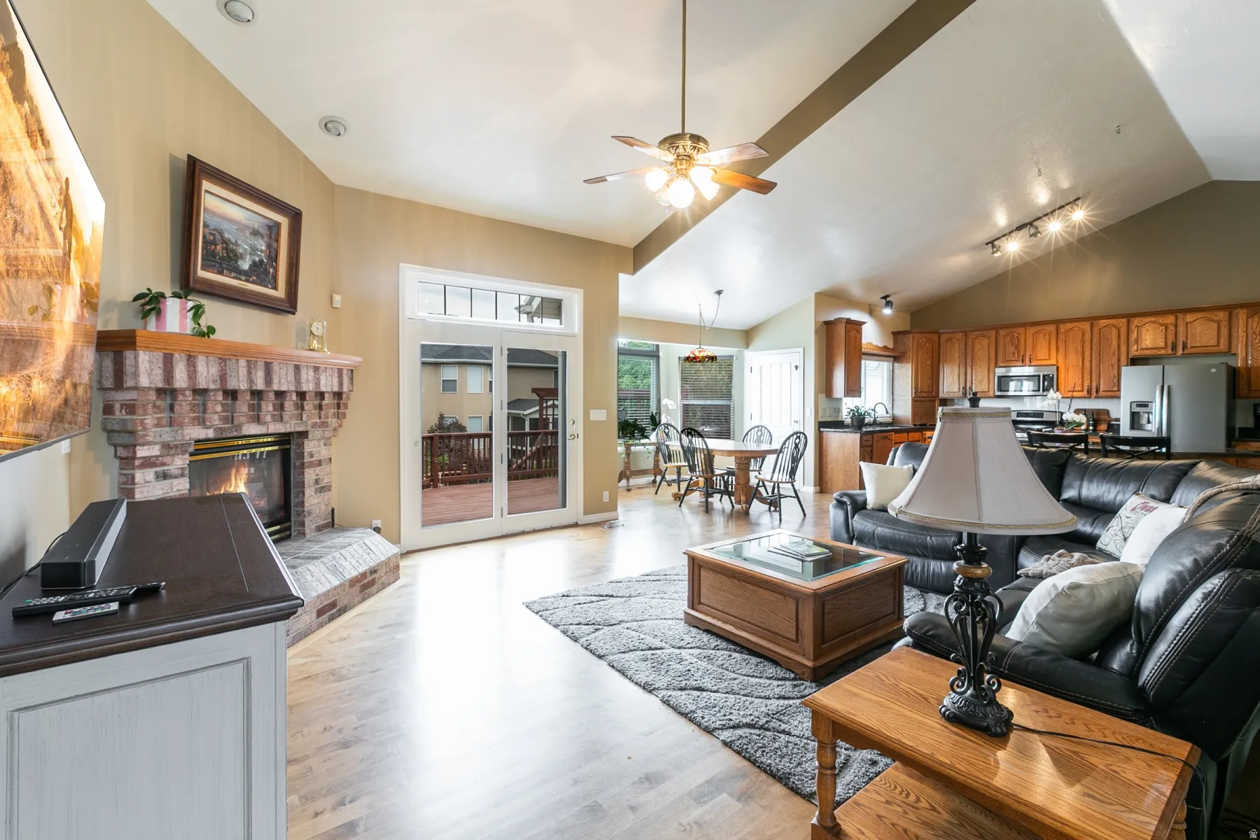 Spacious living area featuring a brick fireplace with a wood mantle, sliding glass doors, vaulted ceilings, and wood-finish flooring