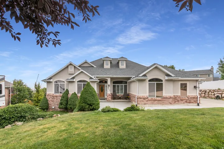 Stucco and stone exterior featuring a covered entry, arched windows, and a dark shingled roof