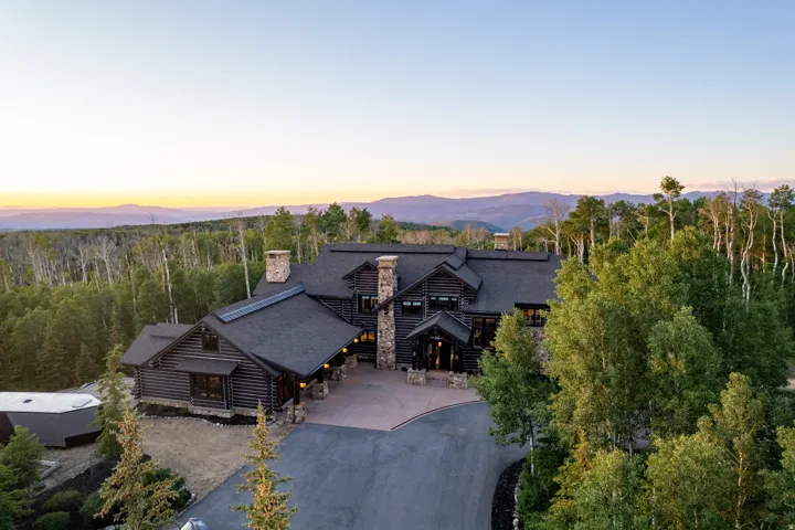 Log home with multiple stone chimneys and a dark shingle roof