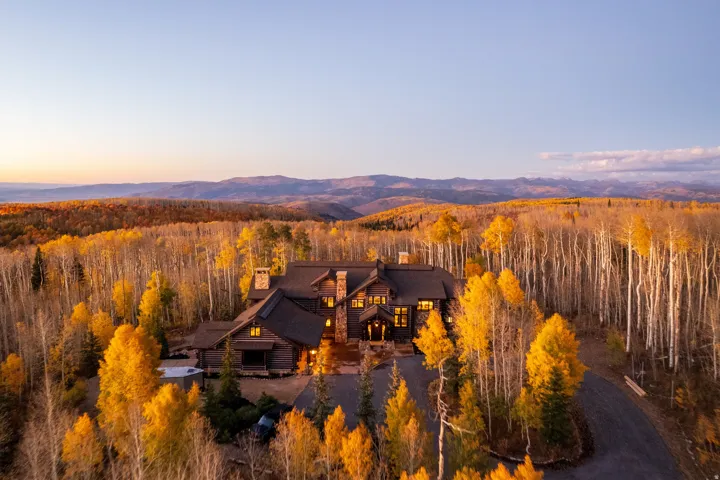 Expansive residential structure with stone chimney detailing, surrounded by extensive natural landscaping