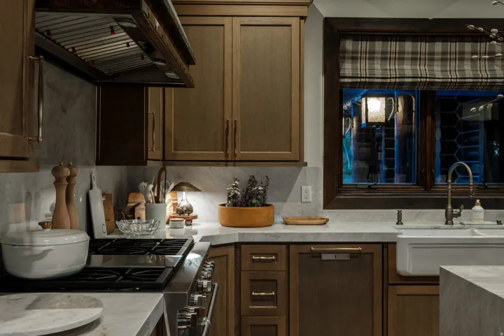 Kitchen featuring wood-finish cabinetry, light-toned countertops, a stainless steel range with overhead ventilation, and a white farmhouse sink