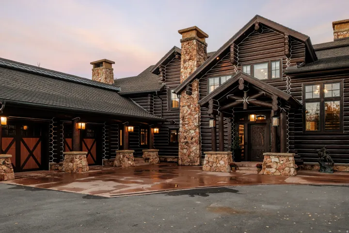 Log-style exterior with stone accents, covered entry, attached garage with wood-paneled doors, and multiple exterior light fixtures