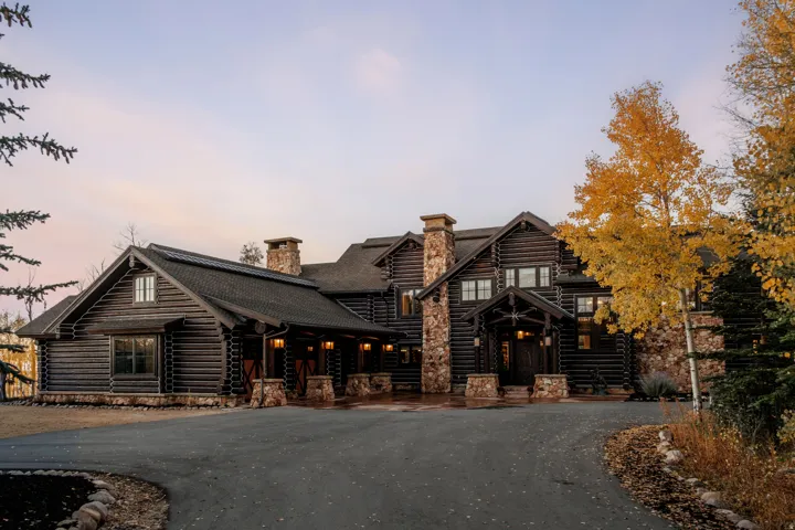 Log cabin exterior with multiple stone chimneys, a covered entry, and a paved circular driveway