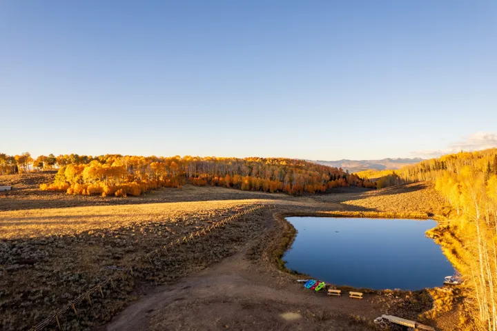 Expansive natural landscape featuring a prominent pond, surrounded by varied topography and extensive tree coverage with golden foliage
