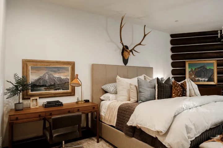 Bedroom featuring a beige upholstered headboard, a wood-finish desk, and a textured log wall detail