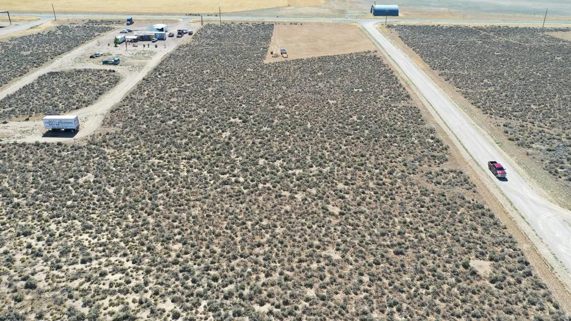 Extensive land parcel featuring natural desert vegetation, a long unpaved road, and distant structures